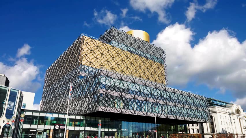 Birmingham, UK  Library of Birmingham, designed by architect Francine Houben. Centenary Square, Broad StreetBIRMINGHAM, UNITED KINGDOM -The Library of Birmingham, Centenary Square,  England, UK, Western Europe, UK. May 5, 2023. A modern building in  UK, with a geometric metallic circle facade and a striking golden cylinder above, set in a plaza with people, flagpoles.