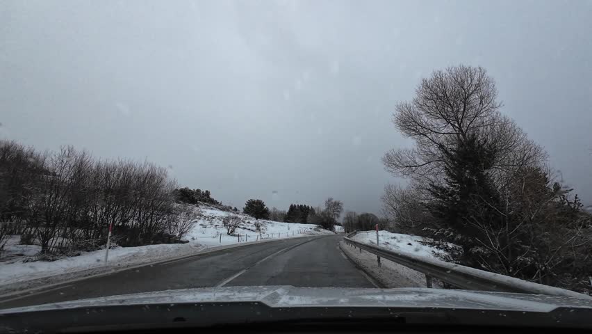 Point of view driving on a winding road through a snowy mountain landscape on a cloudy day