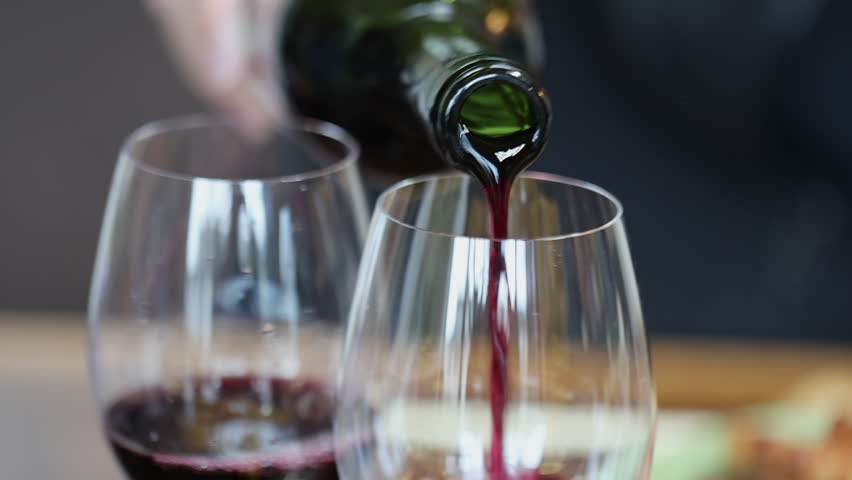 An elegant dinner scene of pouring red wine into a glass.