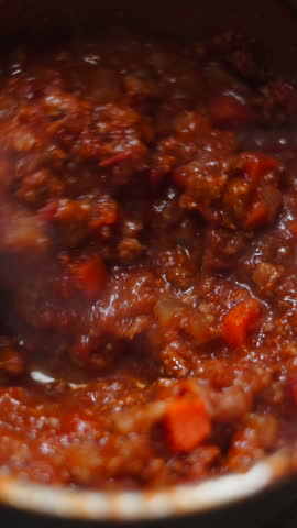 Close up view of a person stirring a steaming, rich bolognese sauce cooking in a pot