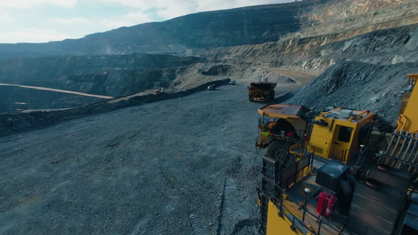 Aerial tracking shot of large excavator loading gold ore to dump truck in open pit mine quarry, aerial fpv.