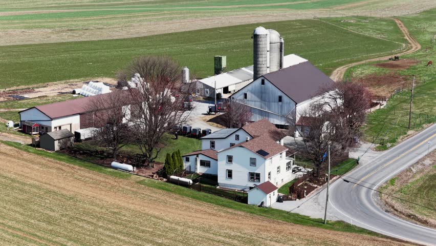 Aerial view of an Amish farm in America with horse drawn buggies parked near barns and silos, rural countryside setting on sunny day reflecting traditional lifestyle and community life. Approach.