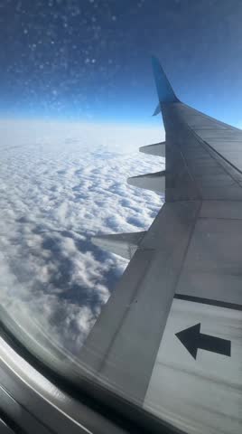 Airplane flying slightly above the clouds. Inside view through the window of an airplane of the wing and turbine. Clouds moving fast below the plane. Airplane flying high, clouds moving below the plane. Travel, exploration, beauty of nature.