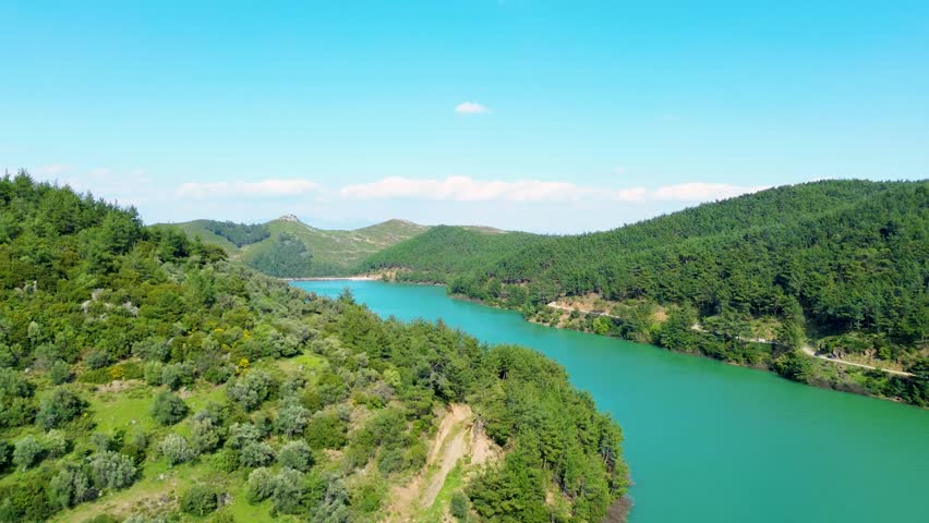 Aerial view of a vibrant turquoise river flowing through dense green forests and rolling hills under a clear blue sky