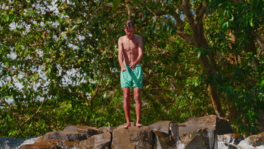 A young athletic teenager jumps from a high, dangerous rocky waterfall, entering the water with his feet. Extreme and dangerous recreation