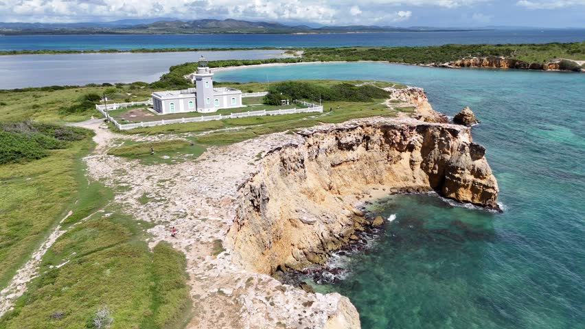 Aerial drone footage of Cabo Rojo lighthouse with rocky coastal cliffs and turquoise ocean in Puerto Rico. Scenic Caribbean landscape featuring rugged shoreline, clear water, and natural coastal terrain.