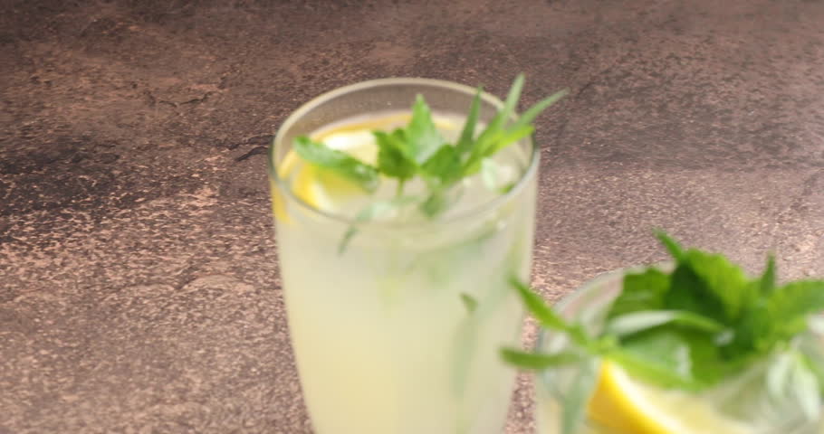 Tasty lemonade with tarragon, mint, ice and lemons on grey table, closeup. Camera moving right
