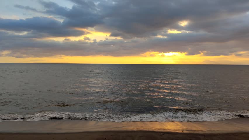 A seascape with calm waves and a sunset obscured by clouds