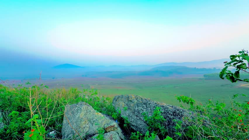 Panoramic landscape of lush green fields and rolling hills covered in morning fog under a clear, colourful sky. Visakhapatnam, India