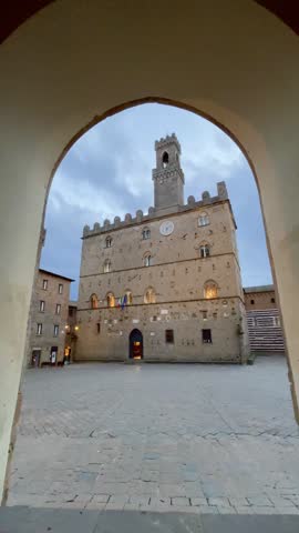 Palazzo dei Priori and medieval architecture in Volterra, Italy, framed by an archway, creating an inviting vista for history, tourism, and European travel during the peaceful twilight hours