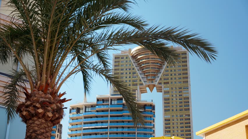 Modern skyscraper architecture with unique golden bridge design against clear blue sky in Benidorm.