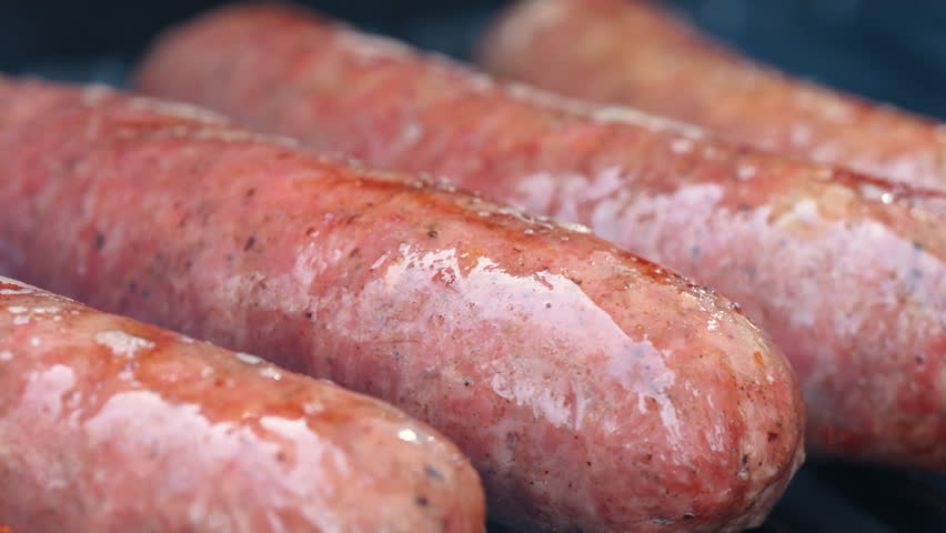 Close up view of Sausages grilling on barbecue with open flame. Close up of juicy meat cooking on grill, outdoor food and summer barbecue