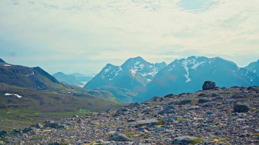 Middagsfjellet, Sandland, Nordkapp, Finnmark, Norway - Two Hikers and Their Dogs Trek Across a Rocky Path With Snow-capped Mountains in the Distance - Static Shot