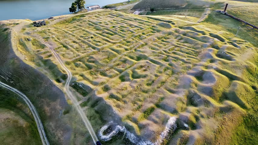 Aerial drone view of the Danube River flowing through the Iron Gates Gorge along the Romania Serbia border. The wide river curves around a forested island, surrounded by agricultural fields and rolling hills