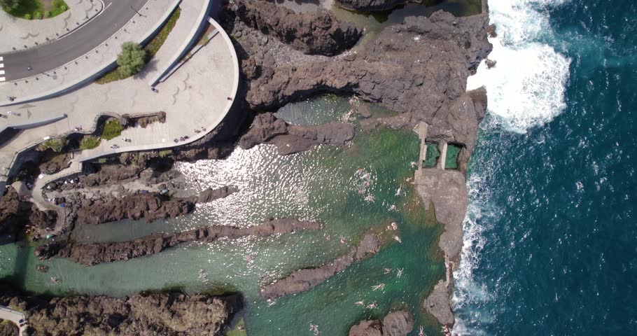 Top-down aerial of swimmers in the crystal clear turquoise water of the volcanic pools.