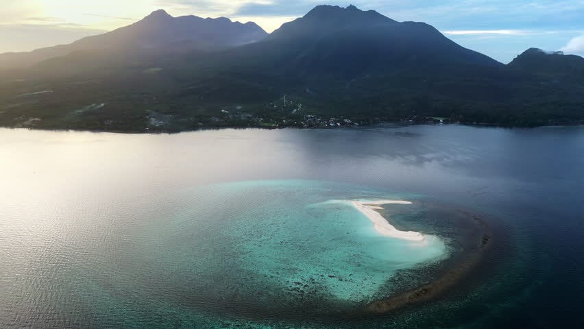 Aerial drone view of a curved sandbar in Coron Bay, Palawan, Philippines, surrounded by calm turquoise waters with dramatic mountain silhouettes in the background