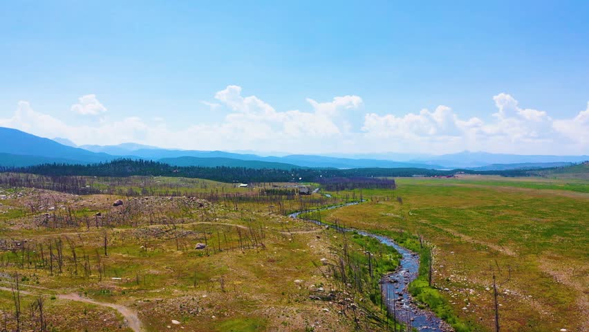 Drone aerial of a Utah mountain meadow landscape with a serpentine creek dry trail network sparse vegetation rustic bridges layered hills and wide western scenery in summer light
