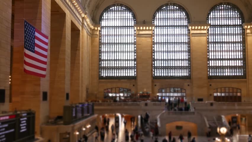 New York Grand Central Terminal on 42 street, United States. Crowd of people inside railway building. American flag, railroad transportation in Manhattan Midtown, NYC. Station interior and passengers.