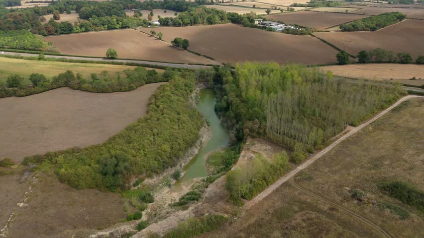 Top down aerial perspective of a deep blue lake enclosed by a steep, high-sided green forest canopy in the English countryside.