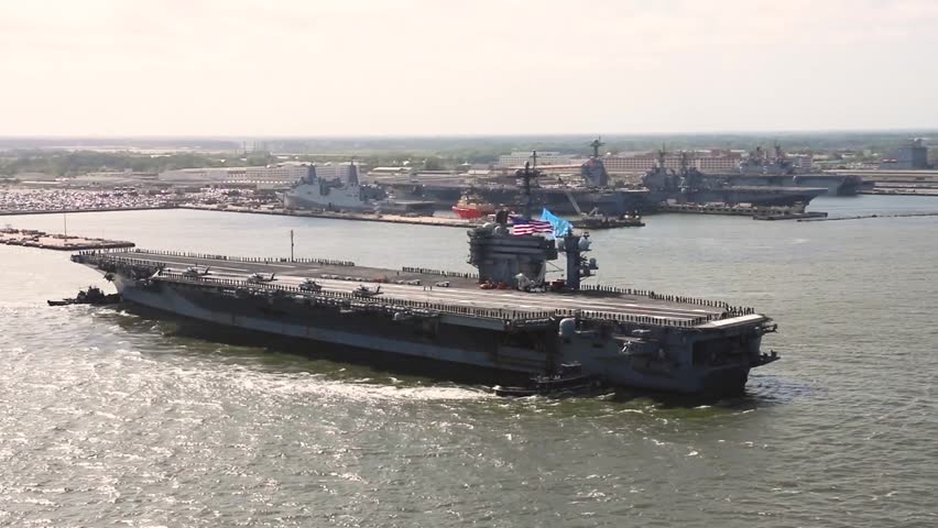 Massive aircraft carrier departs naval base with escort ships, showcasing power, readiness, and strategic maritime dominance globally.