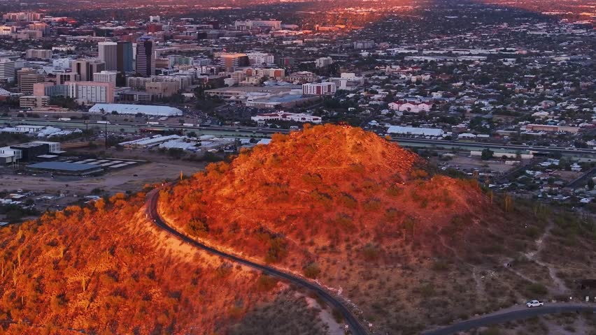 Aerial view of a mountain with a winding road cutting through its terrain, contrasting with the cityscape, Tucson, Arizona, United States.