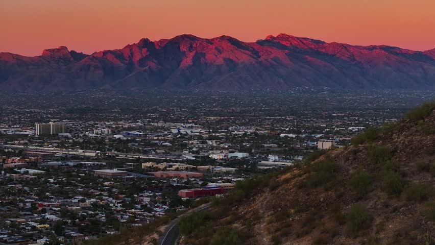 Aerial view of buildings and mountains in the distance, with a warm sunset sky over the vast cityscape, Tucson, Arizona, United States.