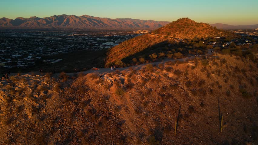 Aerial view of A Mountain with a building atop, glowing in the warm light of sunset contrasting with the dark cityscape below, Tucson, Arizona, United States.