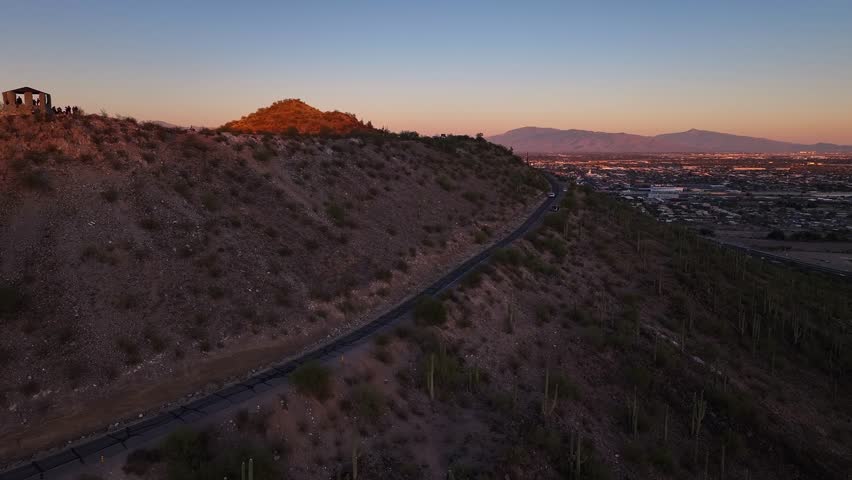Aerial view of A mountain, revealing its shadowed slopes meeting the sunlit side with a winding road, contrasting with the city below, Tucson, Arizona, United States.