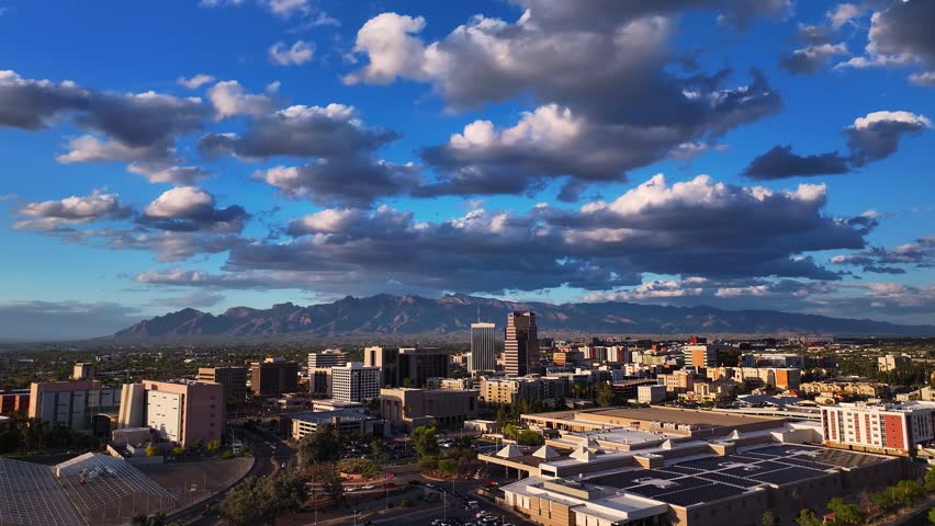 Aerial view of Tucson city buildings under a blue sky with puffy white clouds and distant mountains, Tucson, Arizona, United States.