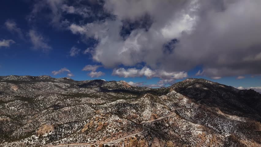 Aerial view of snow dusted rugged mountains meeting winding roads under a sky with scattered clouds, Tucson, Arizona, United States.