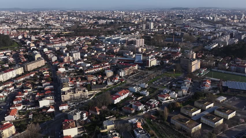 Aerial view of buildings, streets, green trees, and a soccer field, showcasing an urban landscape with a mix of residential and commercial structures, Porto, Portugal.