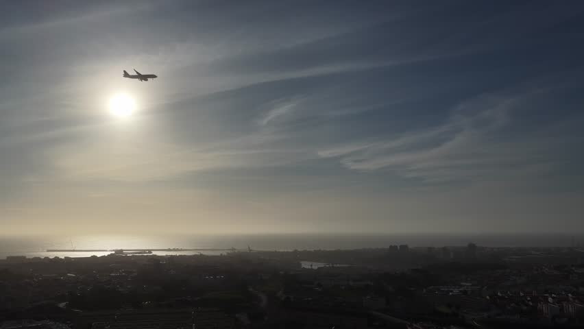 Aerial view of a plane silhouetted against the sun over the cityscape and ocean, casting a soft glow over Porto, Portugal.