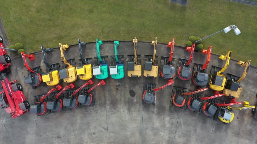 Aerial view of construction vehicles arranged in a semi-circle, displaying a spectrum of vibrant colors against the pavement, Oostkamp, Flanders, Belgium.