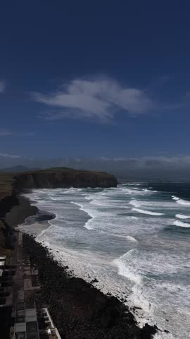 Aerial view of rugged cliffs meeting the foamy waves of the sea, creating a striking contrast of dark rock and white water, Ribeira Grande, Portugal.