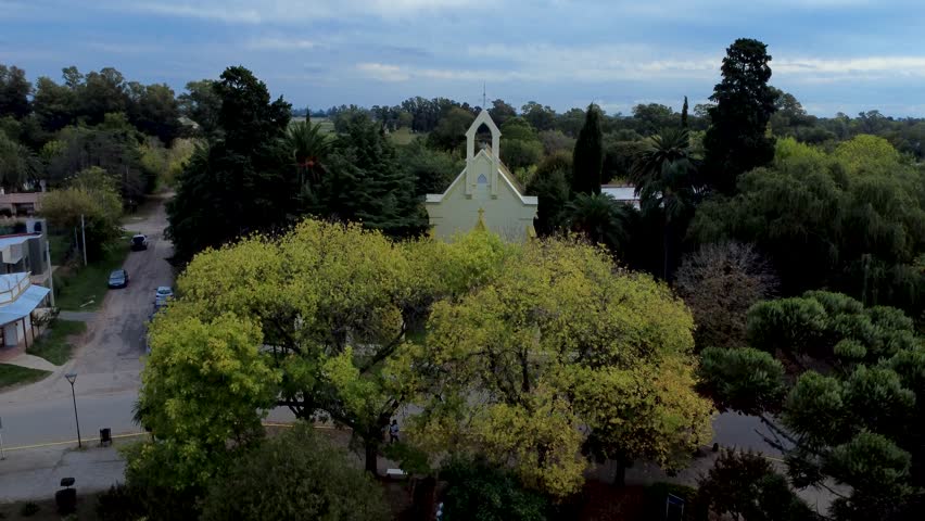 Aerial High-Angle View of a Small Yellow Chapel Surrounded by Lush Green Trees in a Rural Village