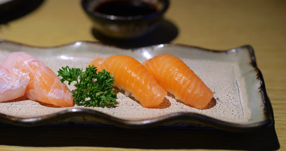 Elegant slow motion showcase of salmon and salmon belly nigiri, featuring delicate fish served on small plate with parsley garnish at Japanese restaurant. Panning close up camera motion
