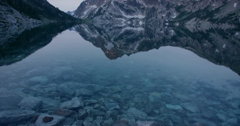 Still Sawtooth Lake Idaho reflecting snow patched mountain peak in calm clear alpine water, establishing medium tilt up