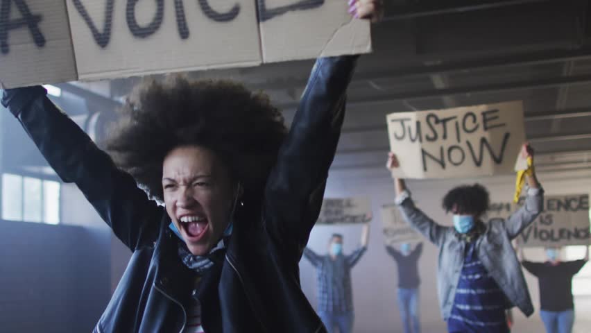 Lead woman raising sign and sparking justice chants under underpass, purple icons overlaying faces. Placards, protest, activism, crowd, urban, street, solidarity