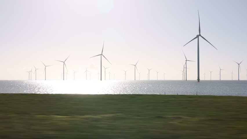 Wide landscape perspective over grass, water and distant turbines with bright morning sunlight.
