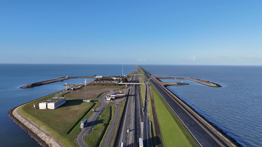 Drone rises above the island road and harbor revealing the dam extending toward faint land on the horizon.