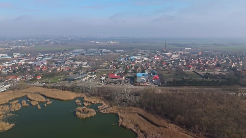 Székesfehérvár, Hungary, industrial suburb and Sóstó Salt Lake with warehouses, factories, gokart track, wetlands, and surrounding fields captured in a wide aerial panorama under a cloudy sky.