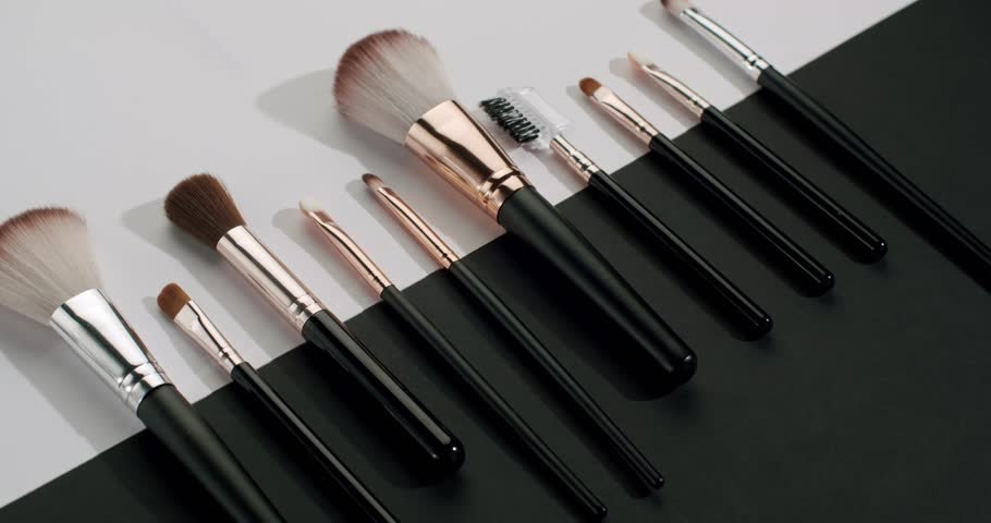 Various professional cosmetic makeup brushes for visage, eyeshadow, blush, and powder laying on a black and white surface in a slow-motion glamour shot, perfect for beauty and skincare concepts