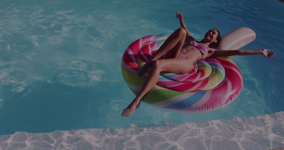 Vertical video: Floating woman in purple bikini stretching arms under sunlight, on lollipop float. Pool, inflatable, poolside, outdoor, sunny, lifestyle, bokeh