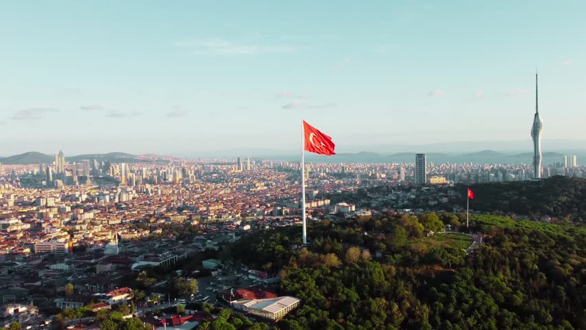 Aerial view of Bosphorus strait with Turkish flag waving, iconic Istanbul landscape showing waterway, bridges and city skyline, captured in daylight highlighting culture, geography and urban beauty.