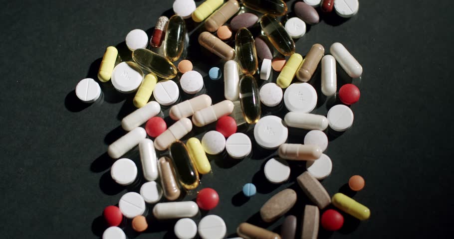 Many different pills, tablets, and capsules falling onto a reflective dark surface, Colorful medication pills and capsules falling on a dark surface