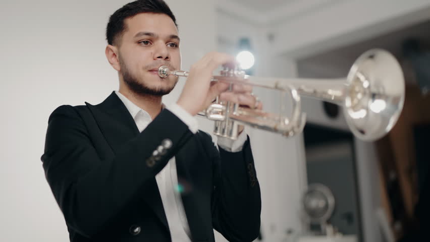 A young and handsome man dressed in a suit plays the trumpet with desire and inspiration. Playing live jazz concert. Passion for music. Close Up hand of young trumpet player. Music room.