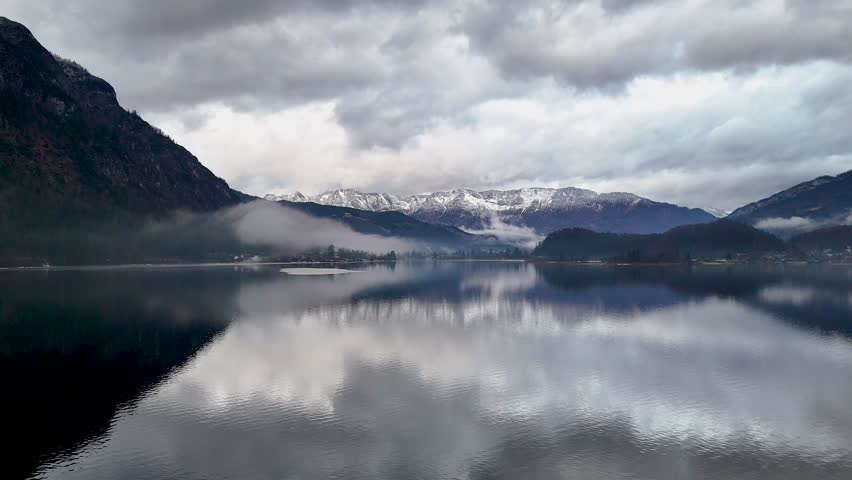 Majestic alpine landscape featuring a calm lake reflecting moody clouds and snow capped mountains