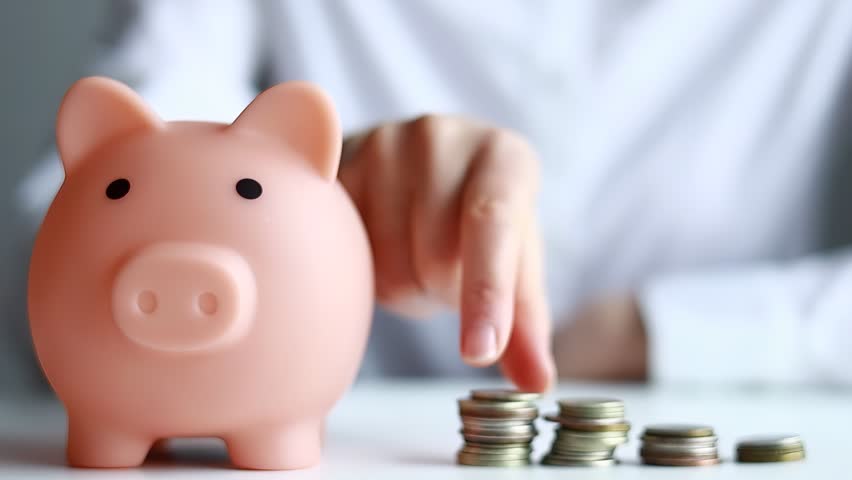 Saving coins in a piggy bank at a desk during the day.