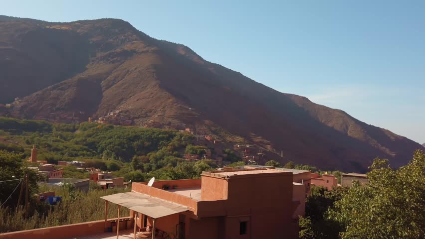 Imlil village in Morocco’s High Atlas Mountains features traditional Berber terracotta buildings nestled on a hillside amid arid landscape and greenery, seen from an elevated panoramic perspective.