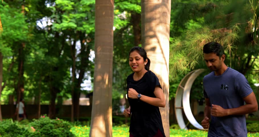 Indian young couple jogging in park together enjoying healthy morning routine and fitness oriented start of the day, spending quality time outdoors breathing fresh air surrounded by trees
